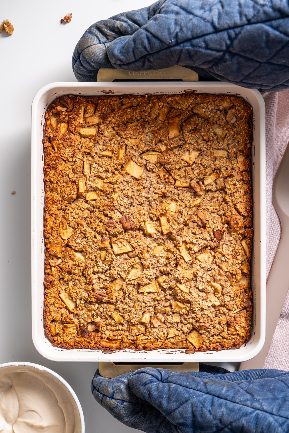 Whole baked apple pie oats in a white baking dish before slicing.