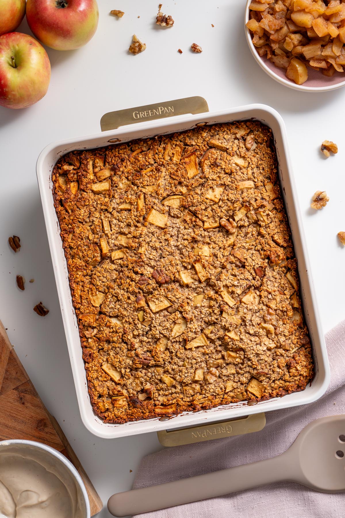 Overhead view of apple pie baked oats in a baking dish surrounded by apples and stewed apple topping.