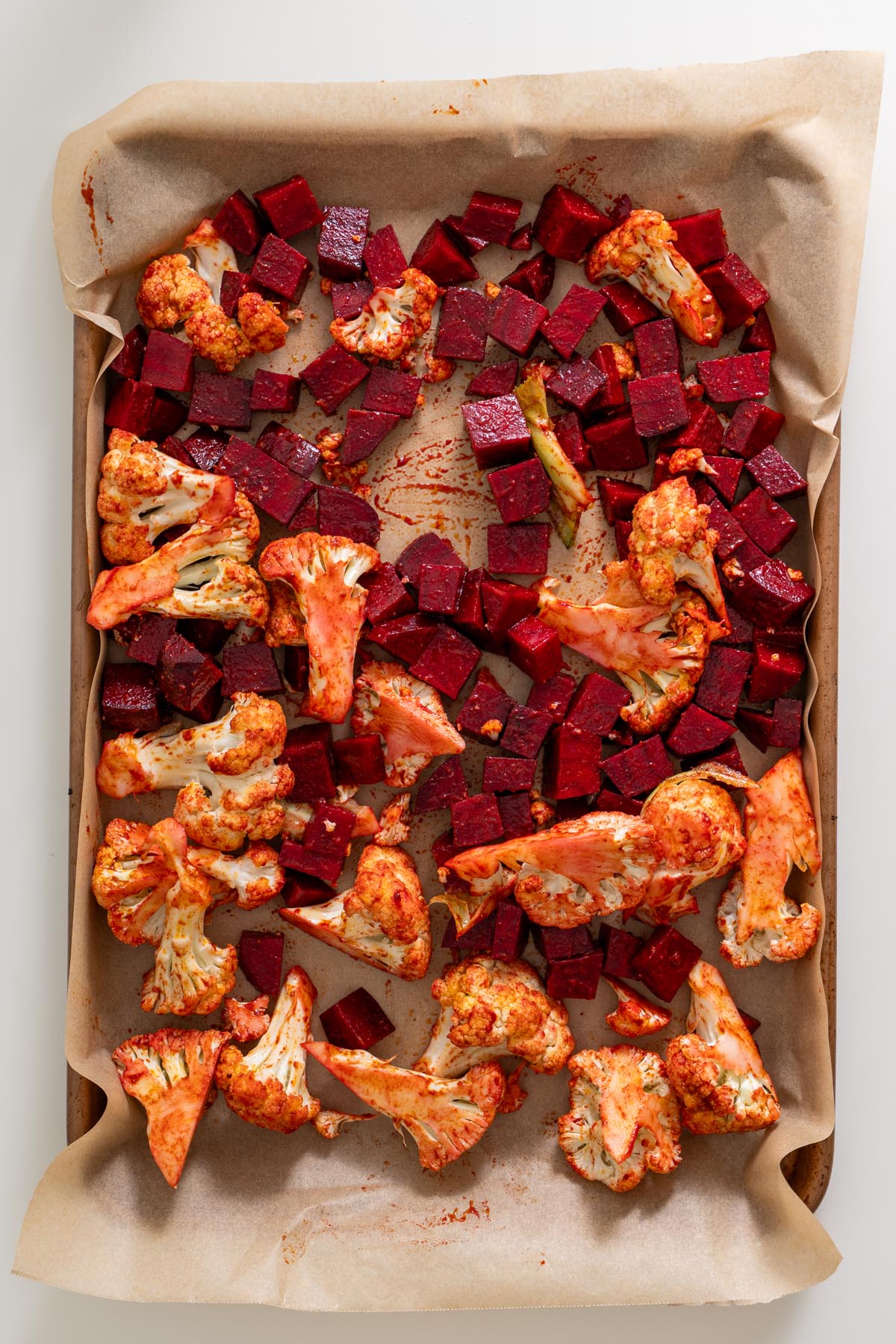 Roasted cauliflower and beetroot coated in harissa on a parchment-lined baking tray before baking