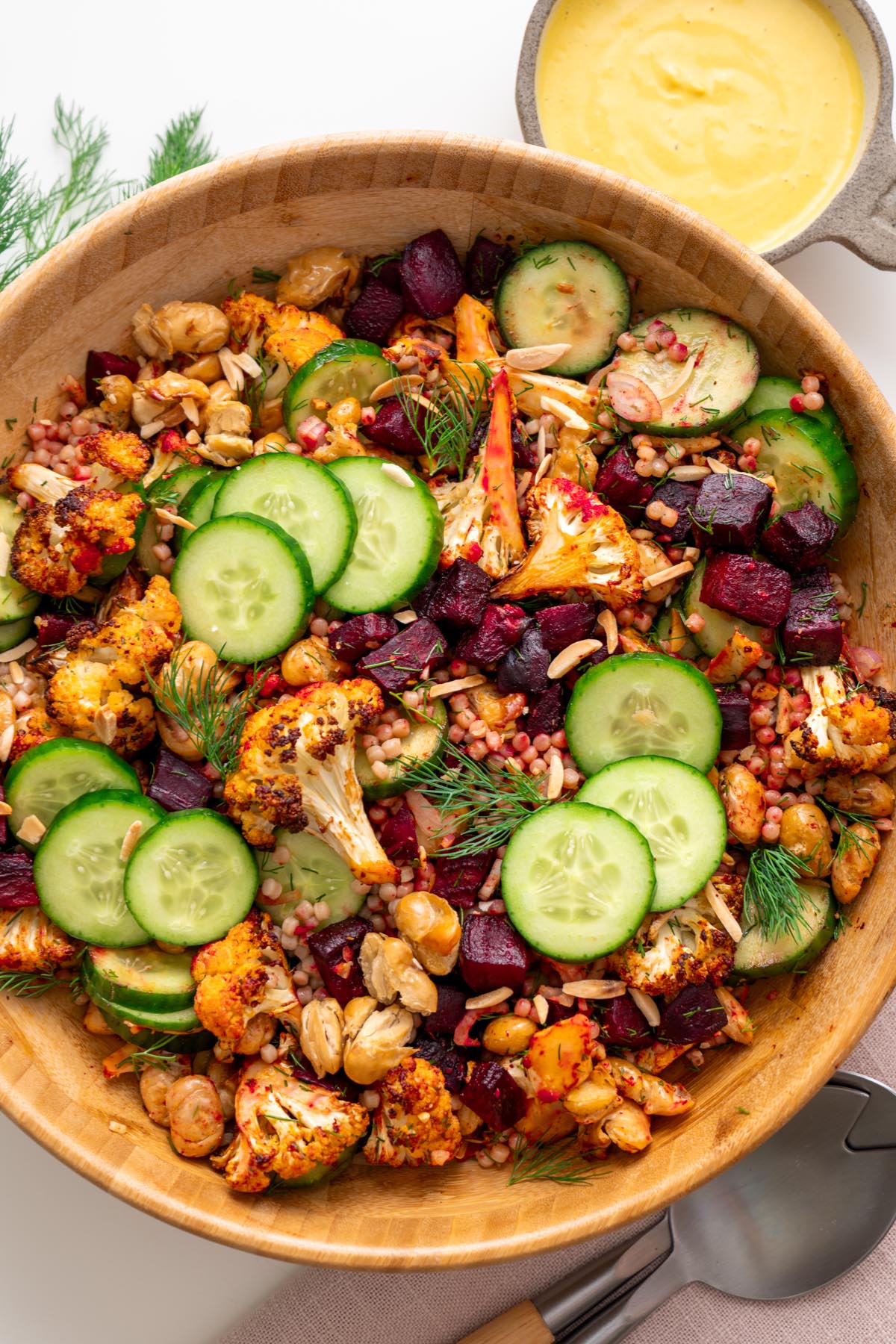 Vibrant harissa cauliflower beetroot salad with cucumber, butter beans, and dill served with a small bowl of golden dressing on the side