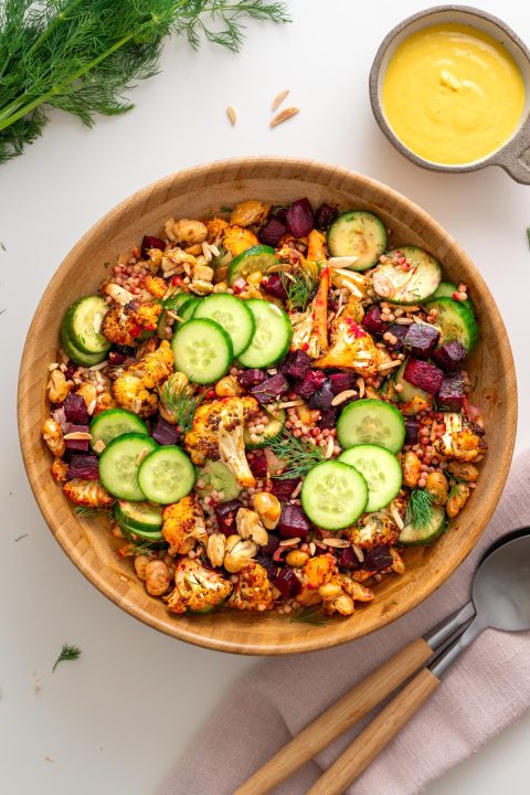 Overhead view of harissa cauliflower beetroot salad in a wooden bowl with tahini turmeric dressing and fresh dill on a white surface