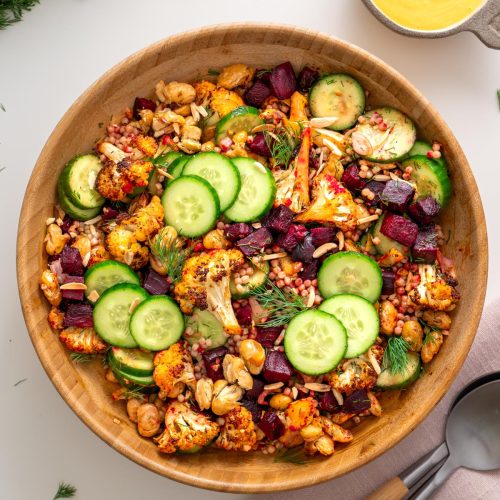 Overhead view of harissa cauliflower beetroot salad in a wooden bowl with tahini turmeric dressing and fresh dill on a white surface