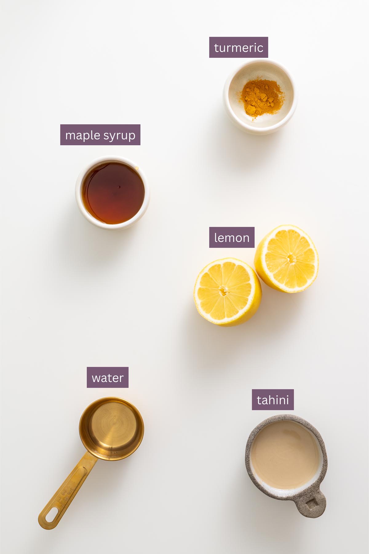 Vibrant dressing ingredients for tahini turmeric sauce on a white surface, including tahini, lemon, maple syrup, turmeric, and water