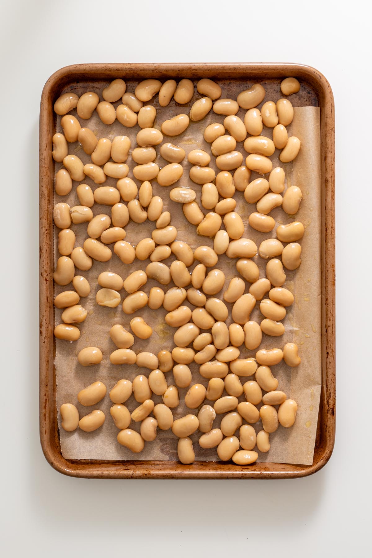 Uncooked butter beans spread on a parchment-lined baking tray before roasting
