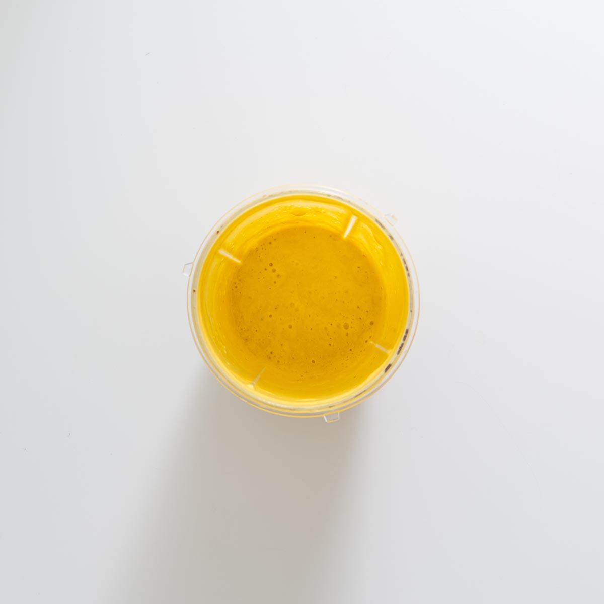 Blended golden tahini turmeric dressing in a small blender cup on a white background
