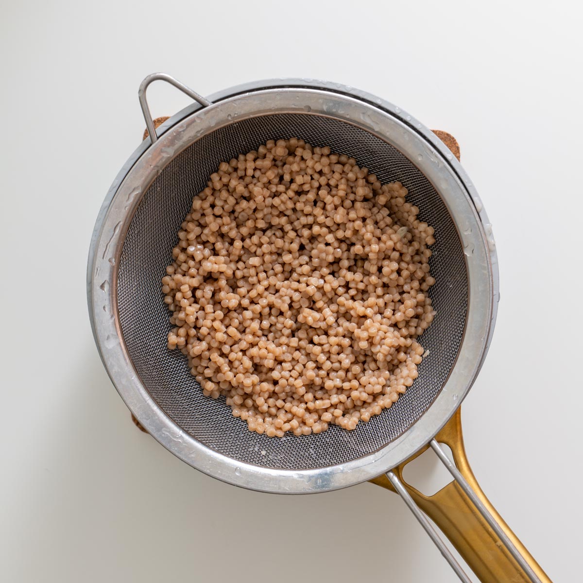Close-up of cooked pearl couscous draining in a fine mesh strainer