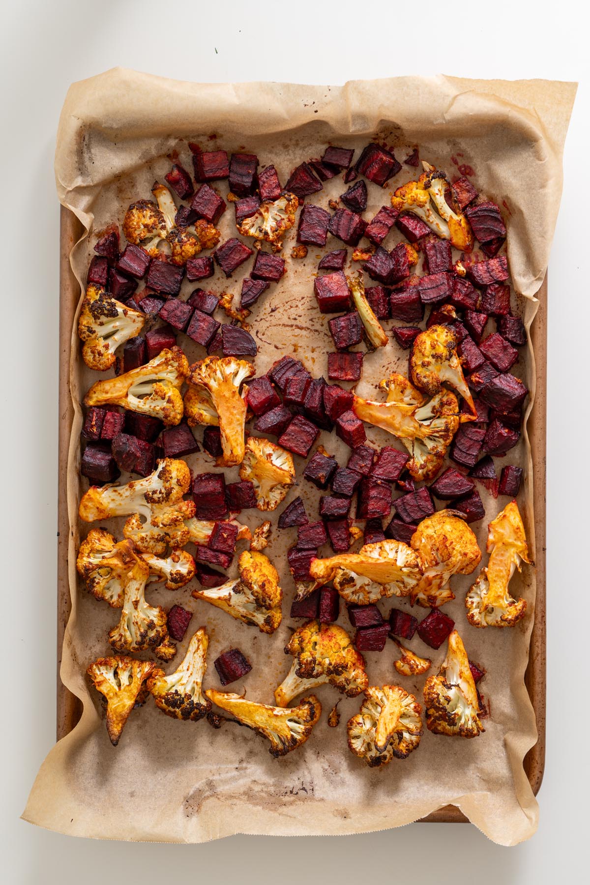 Roasted cauliflower and beetroot on a parchment-lined tray, golden and caramelized after baking