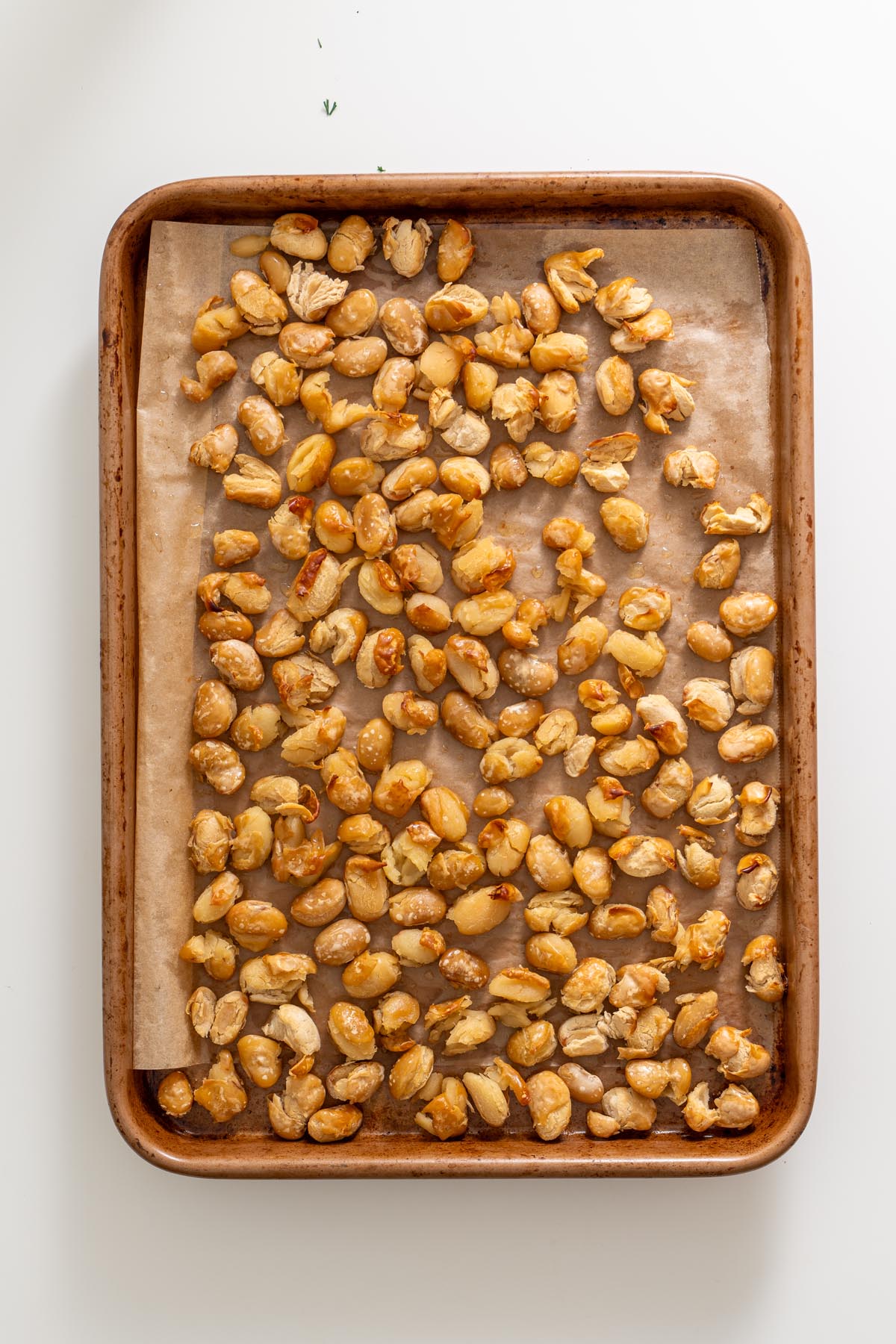Golden roasted butter beans on a parchment-lined baking tray