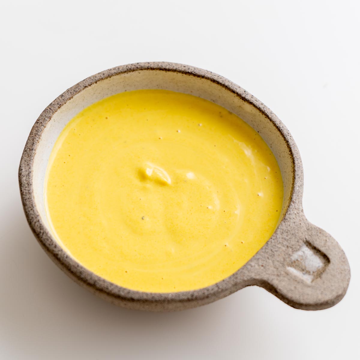 Bright yellow tahini turmeric dressing in a small ceramic bowl on a white background