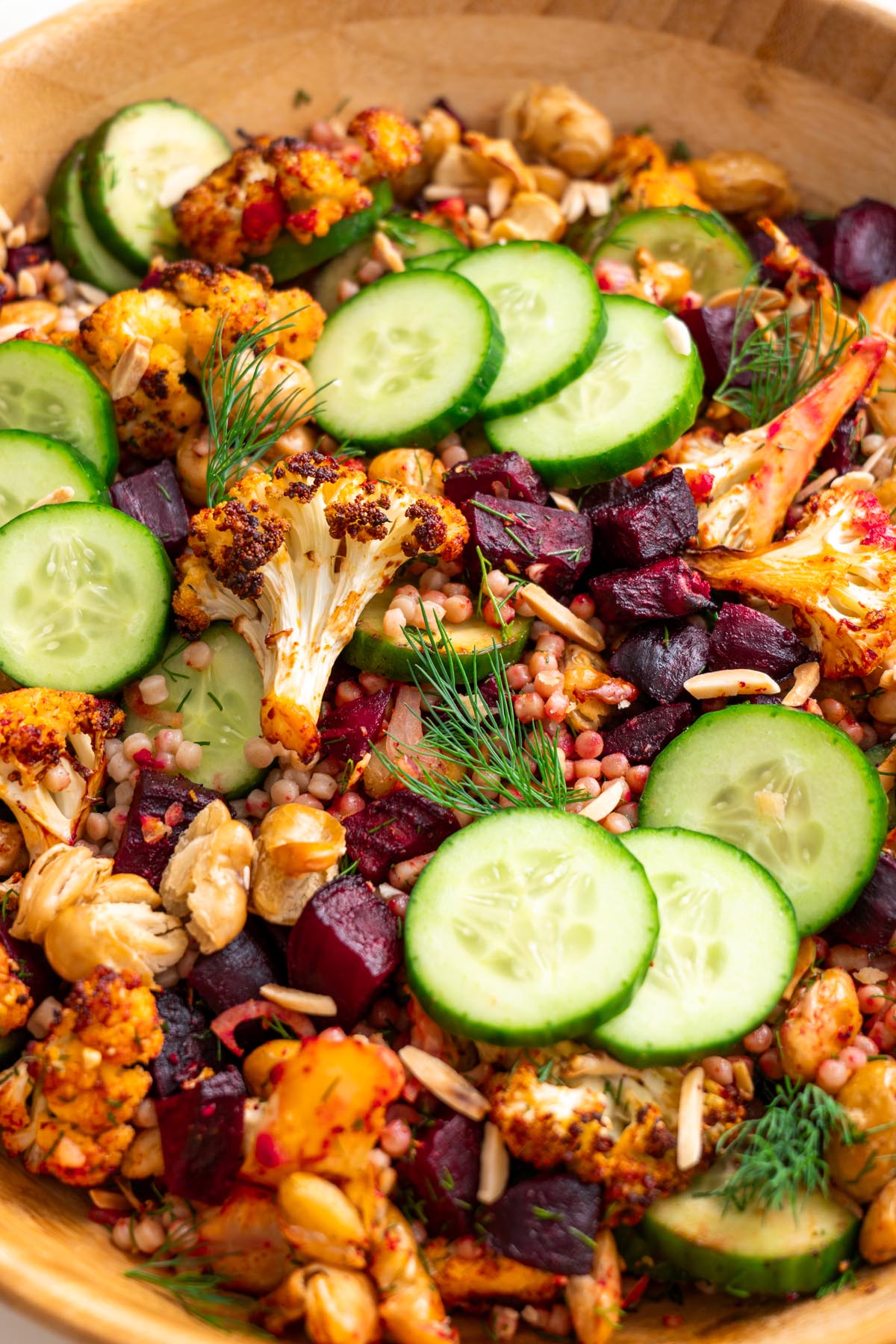 Close-up of roasted cauliflower, beetroot, cucumber, butter beans, and couscous salad garnished with dill in a wooden bowl