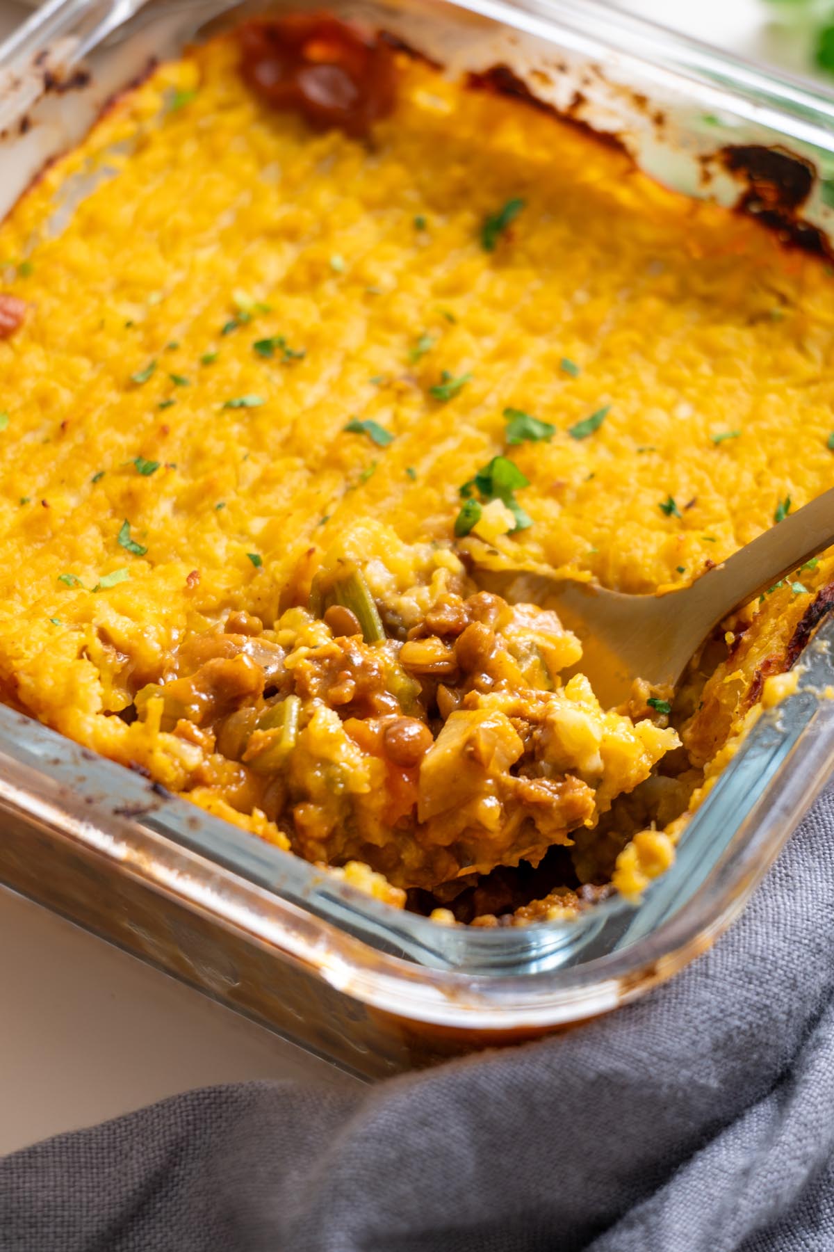 close up of baked shepherds pie with a spoon scooping the lentil filling