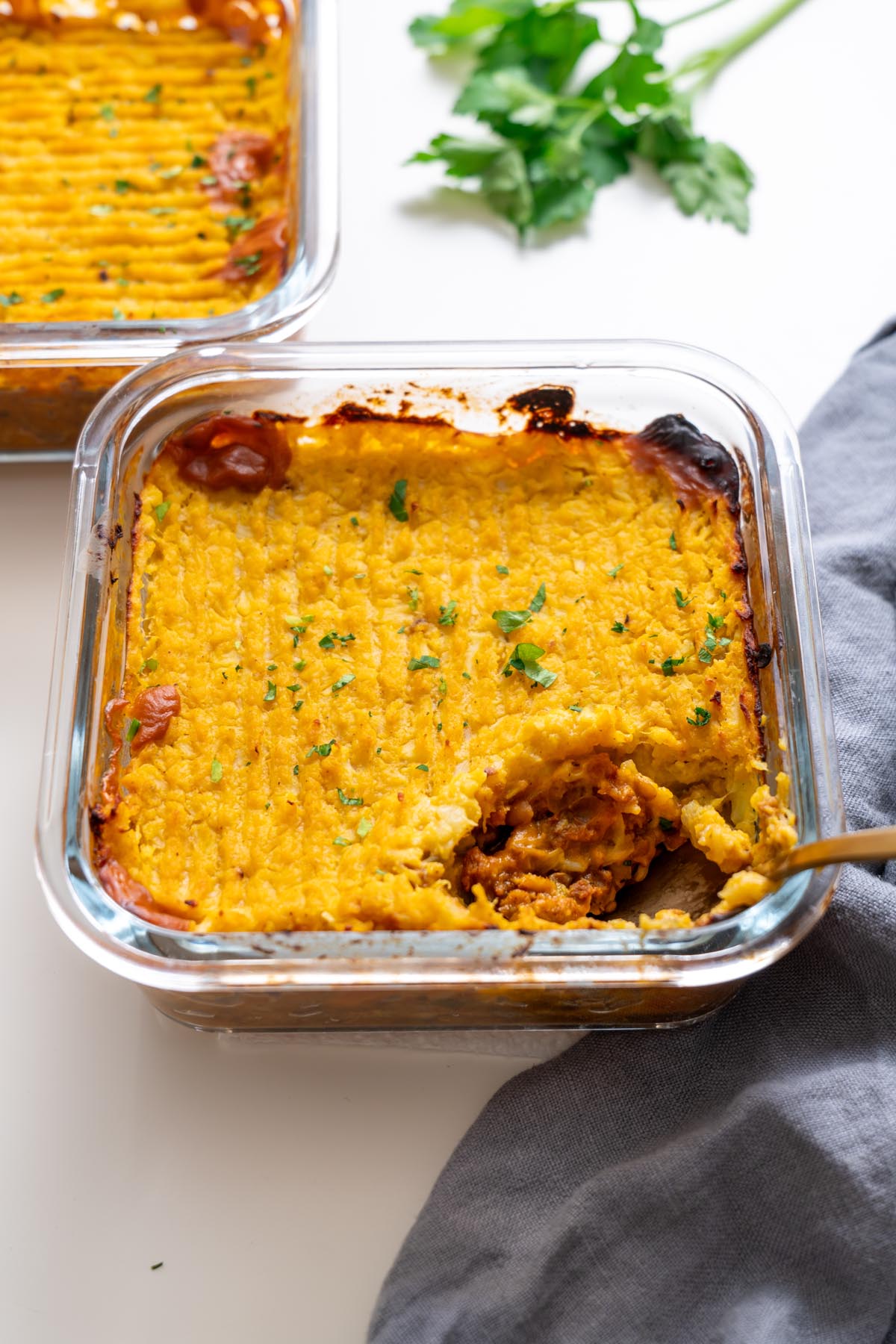 close up of golden baked shepherds pie in a glass dish with a spoonful removed
