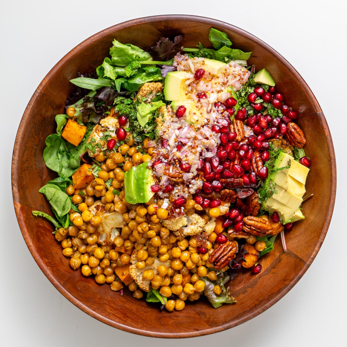 Các nguyên liệu làm món salad phong dành cho lễ hội được sắp xếp thành từng phần trong một chiếc bát gỗ – đậu xanh nướng, bơ thái hạt lựu, hạt lựu, kẹo hồ đào, rau củ nướng và rau xanh