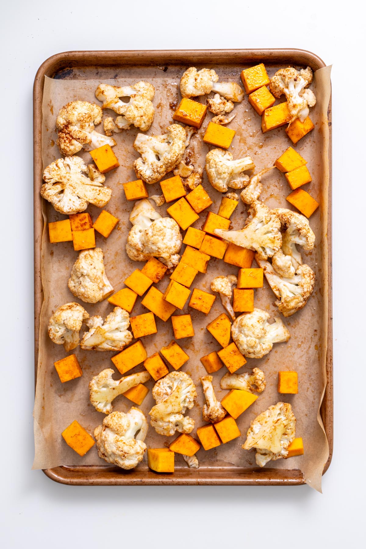 Diced butternut squash and cauliflower tossed with spices on a baking tray ready for roasting