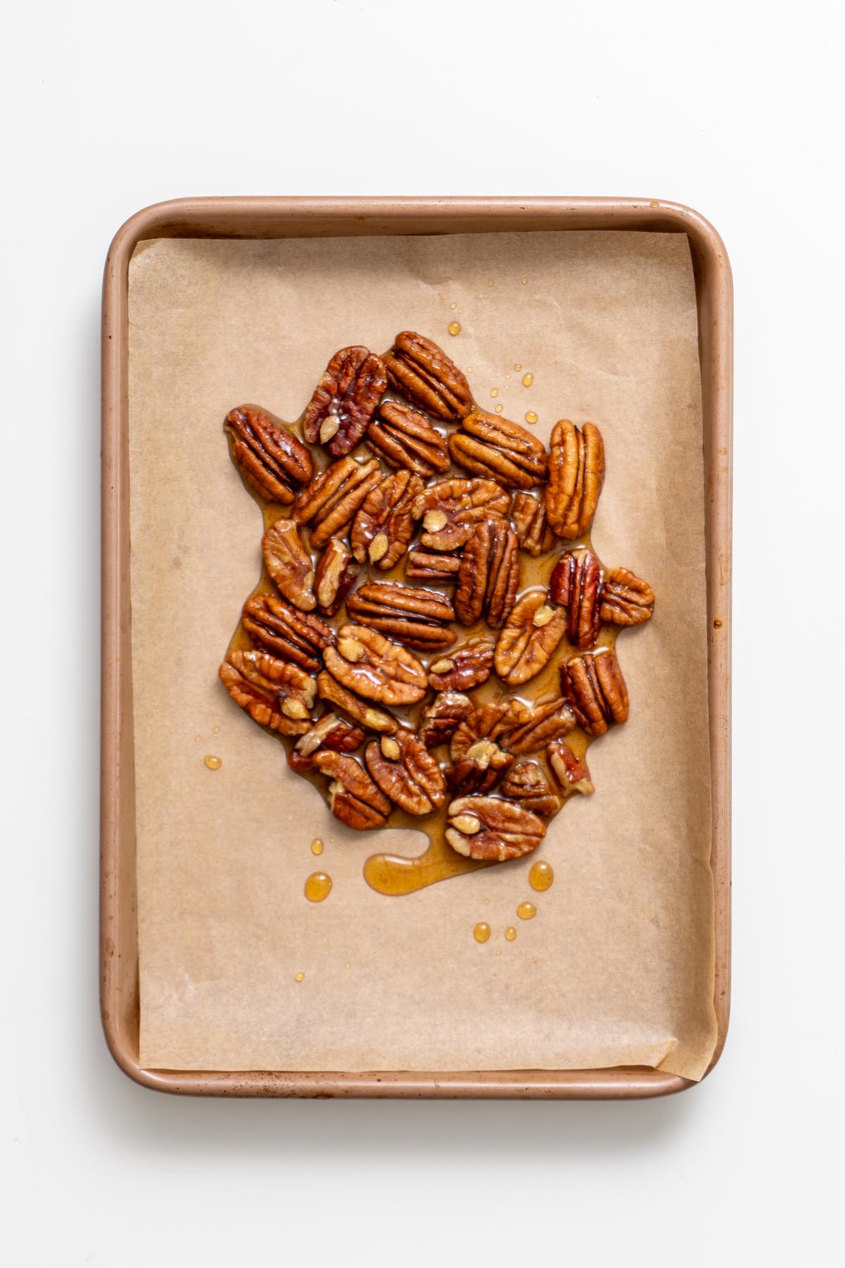 Candied pecans spread on a parchment-lined baking tray with a few drops of syrup