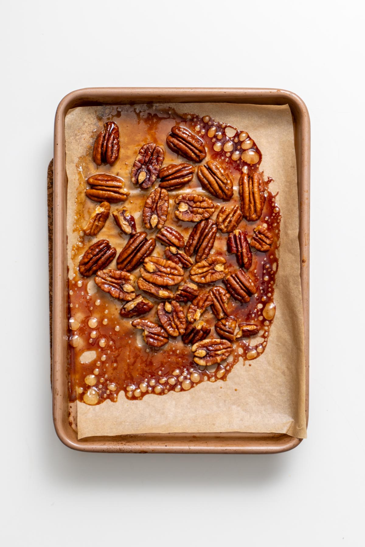 Maple-coated pecans cooling on a baking tray lined with parchment paper