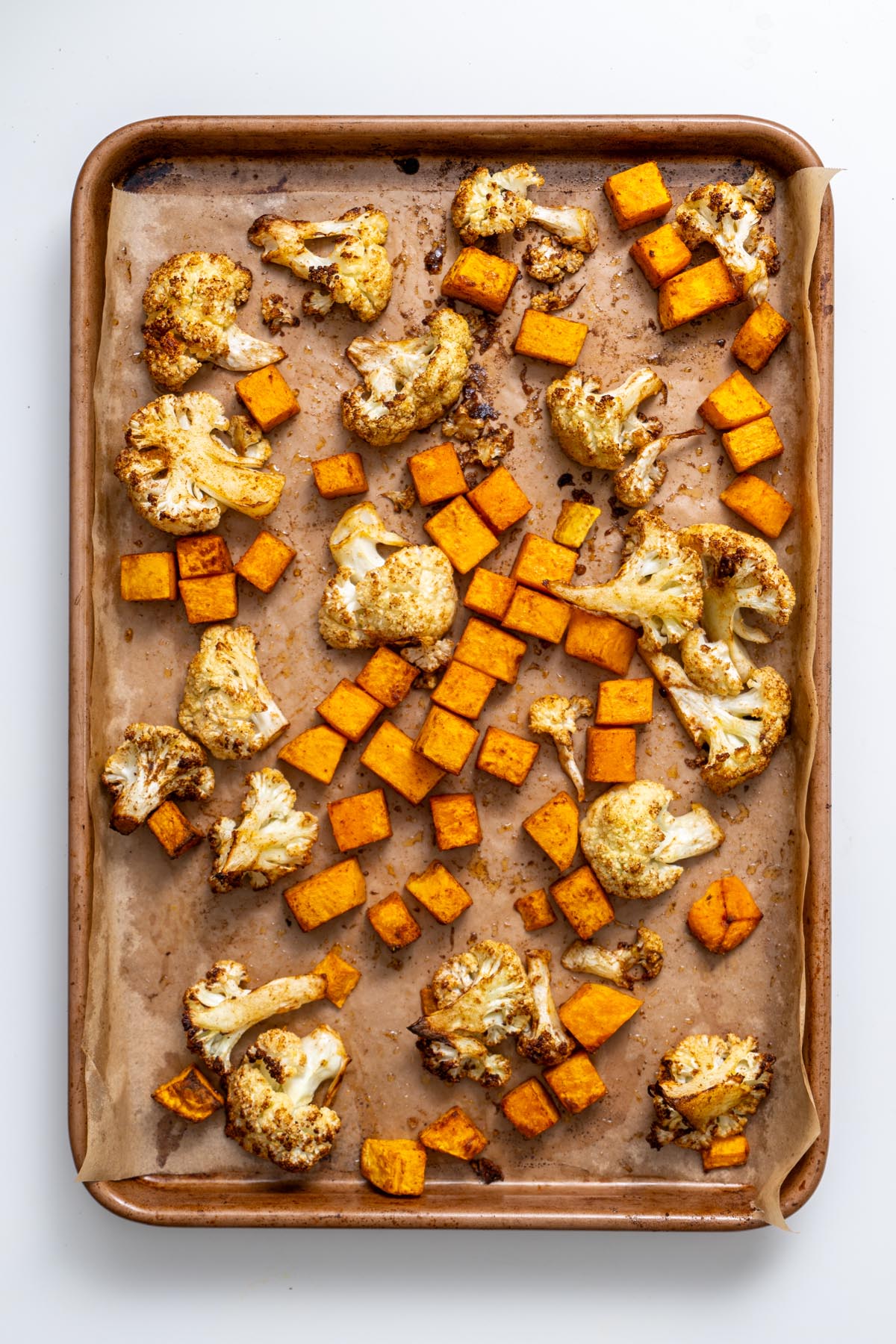 Roasted cauliflower florets and diced butternut squash on a baking sheet lined with parchment paper