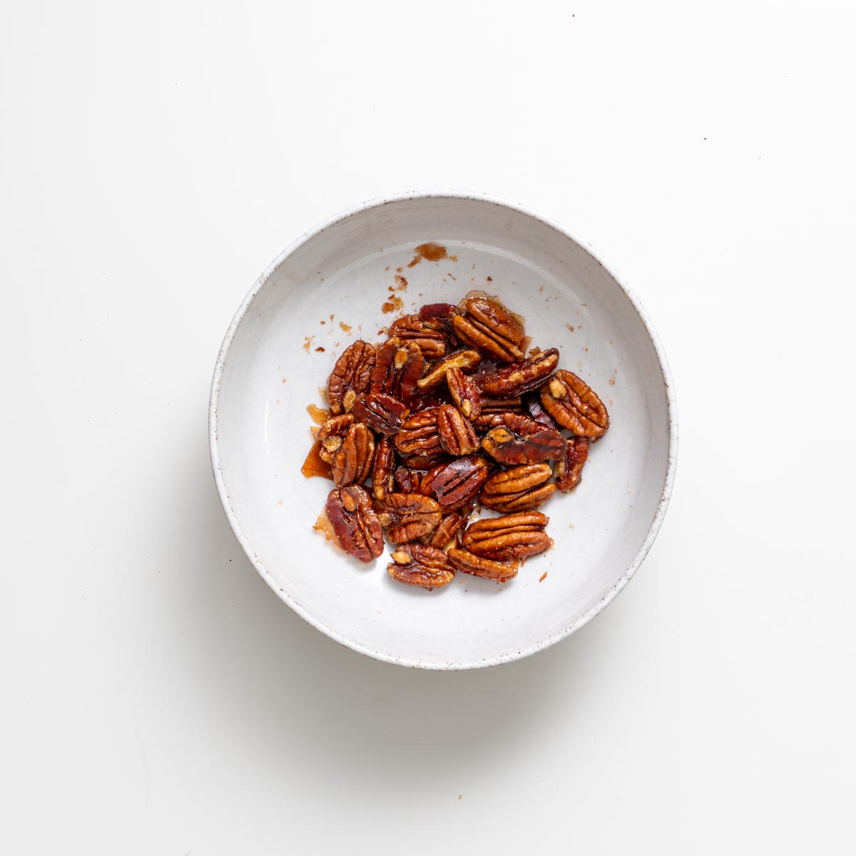 Candied maple pecans in a small white bowl on a white surface