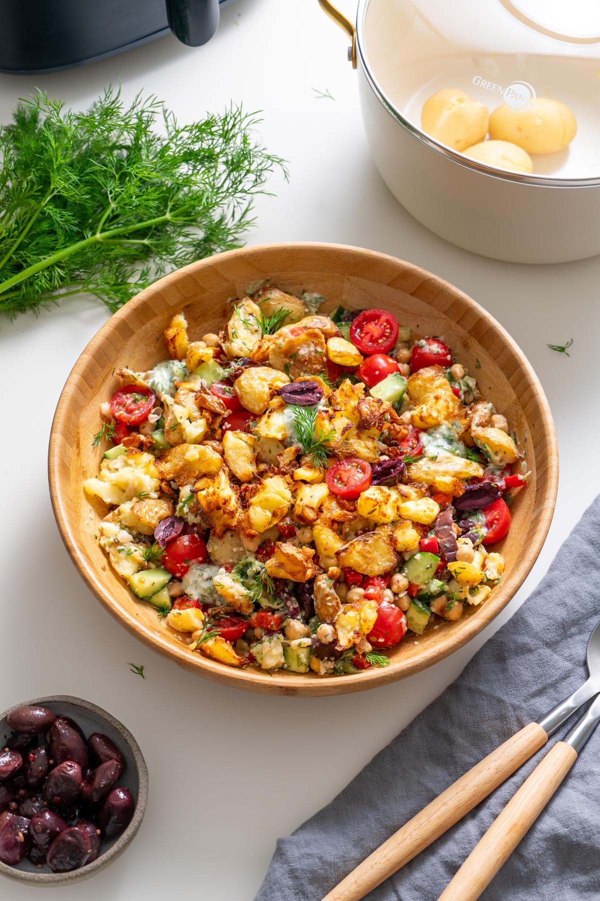 Greek-style crispy potato salad with tzatziki in a wooden bowl garnished with fresh dill and tomatoes.