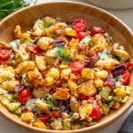 Greek-style crispy potato salad with tzatziki in a wooden bowl surrounded by dill and kitchenware.