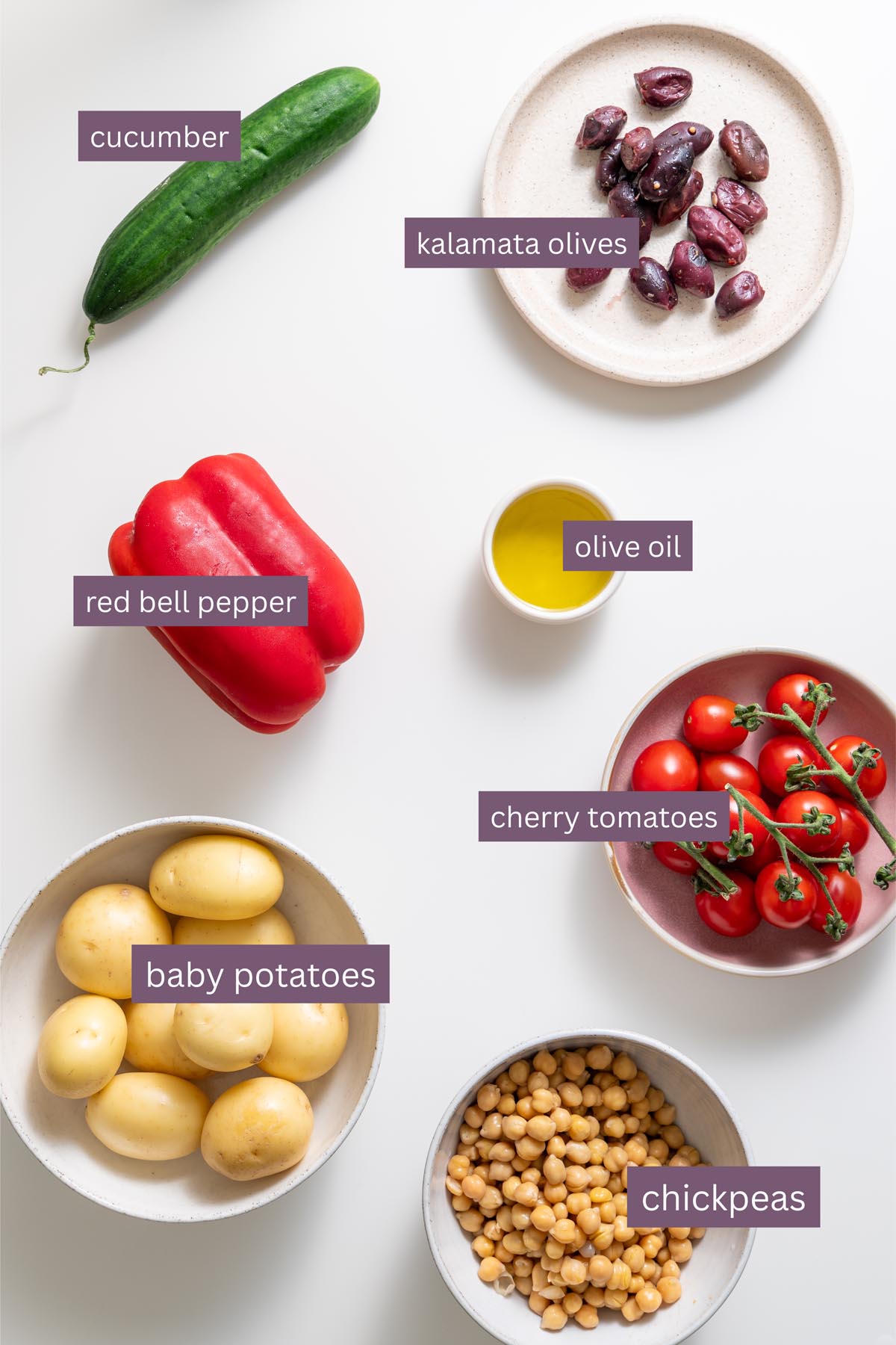 Vibrant ingredients for a Greek-style crispy potato salad with tzatziki on a white surface.