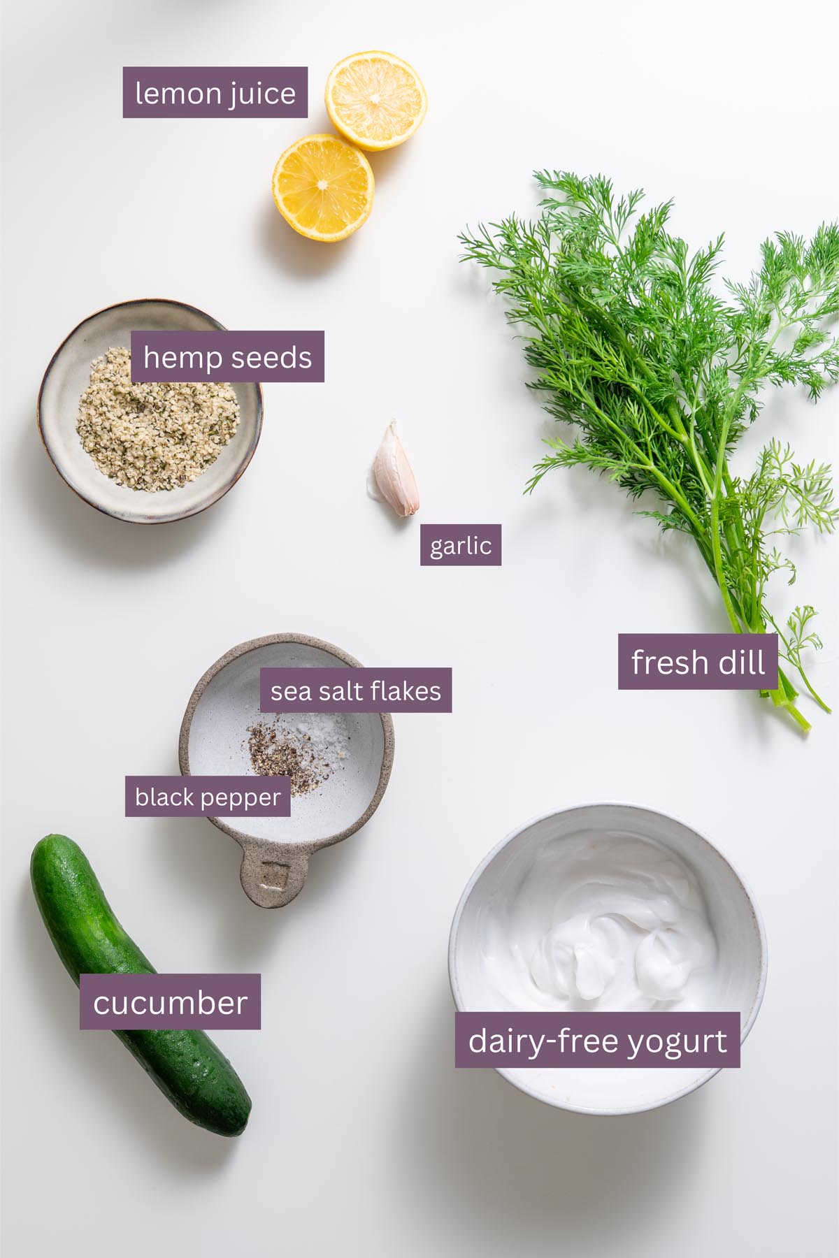 Fresh ingredients for the tzatziki sauce including lemon, dill, garlic, and yogurt on a white surface.