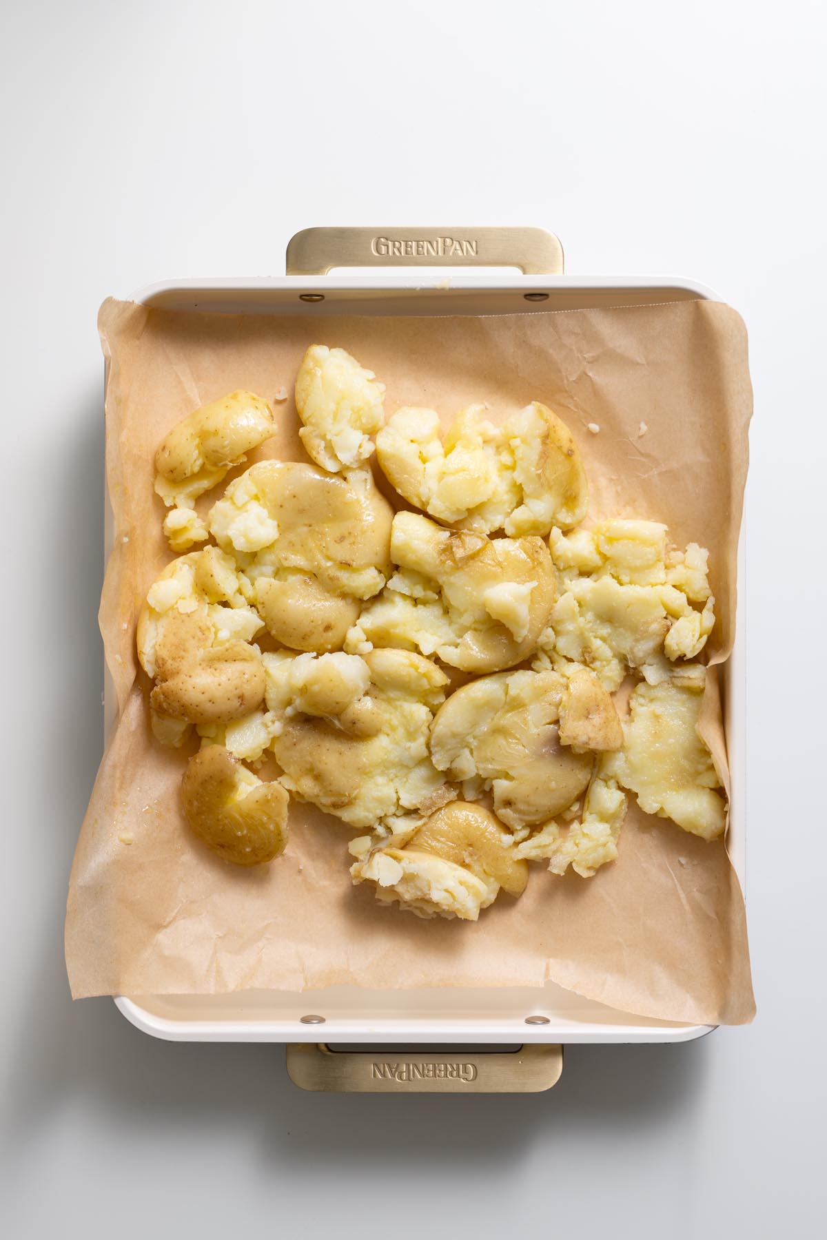 Smashed baby potatoes on a baking tray lined with parchment paper before air frying.