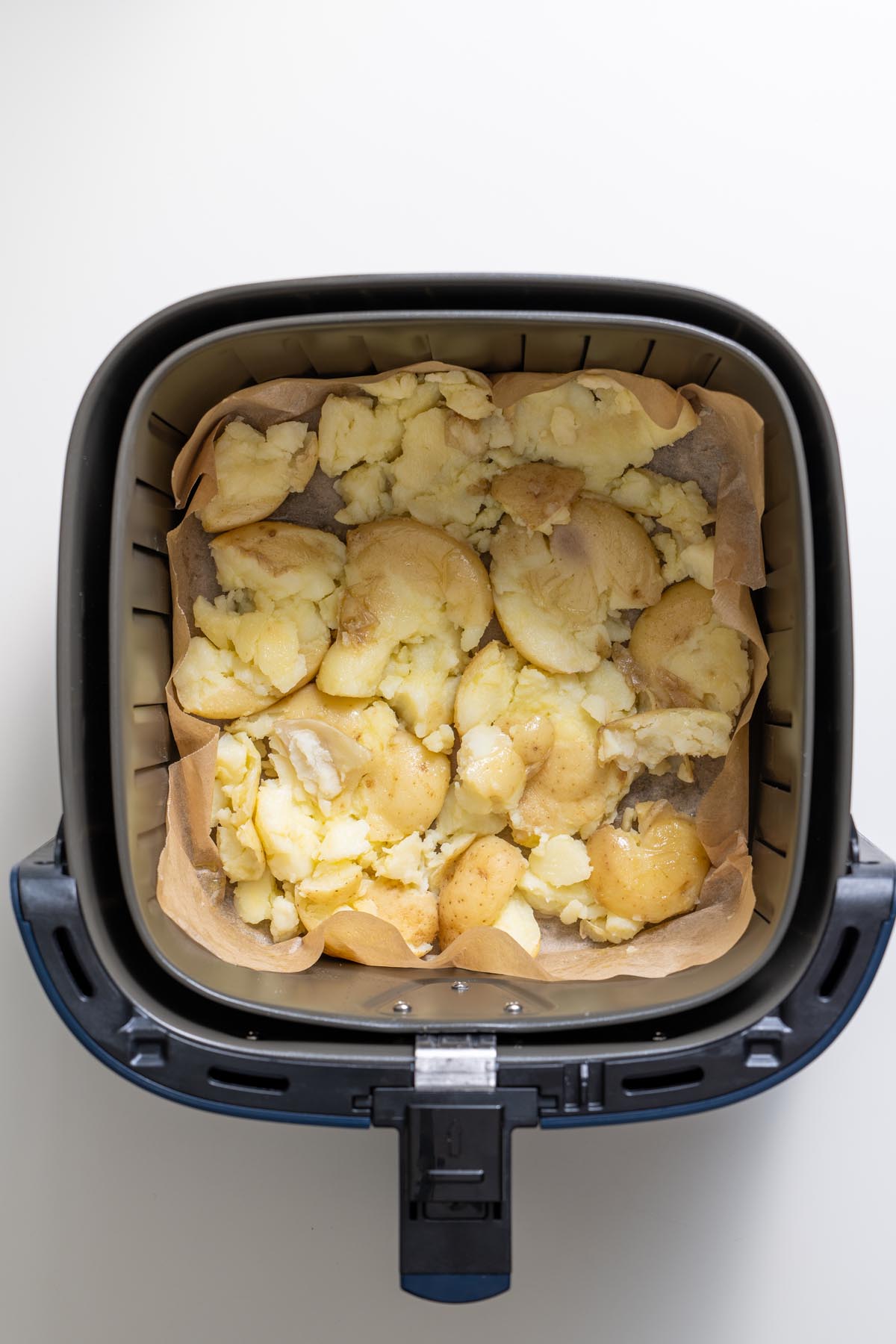 Smashed baby potatoes in the air fryer basket lined with parchment paper before cooking.