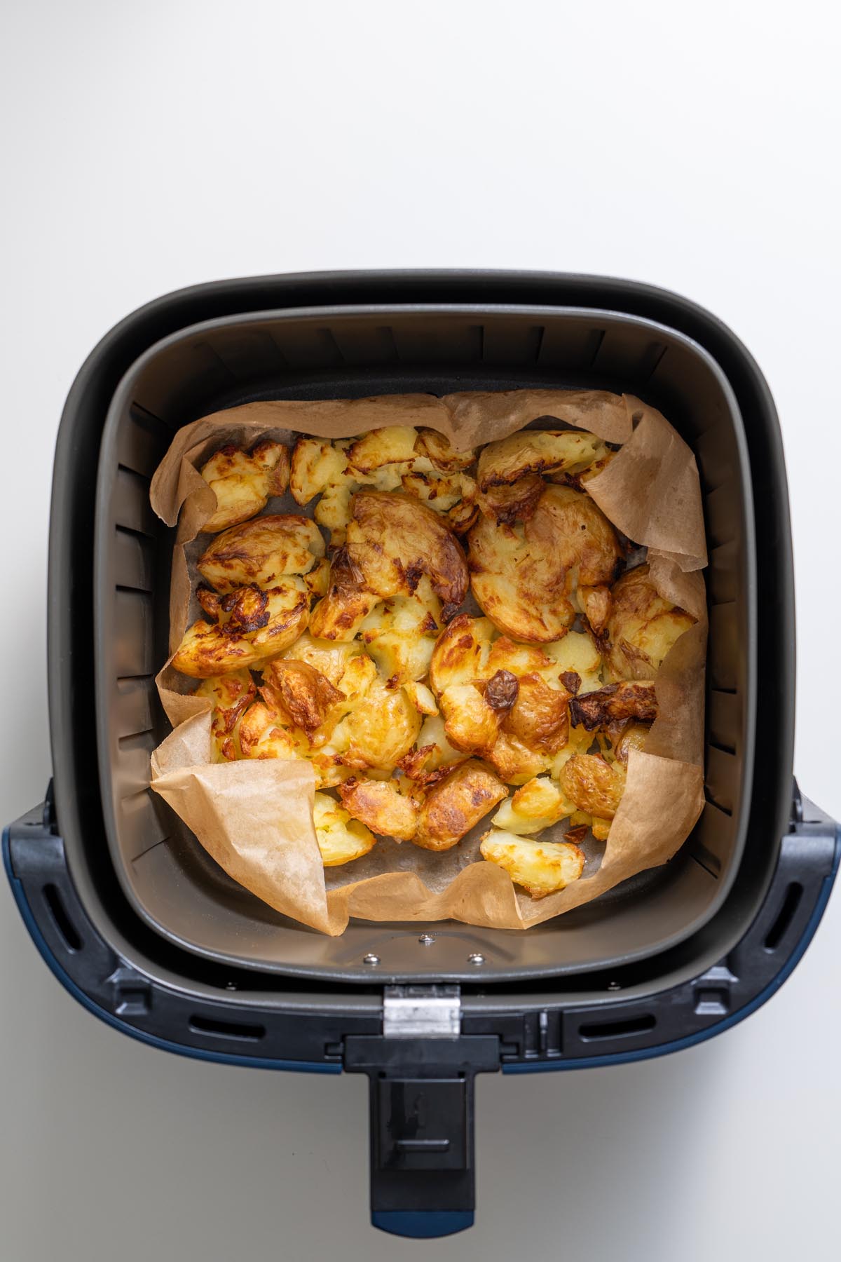 Golden crispy smashed potatoes in the air fryer basket after cooking.