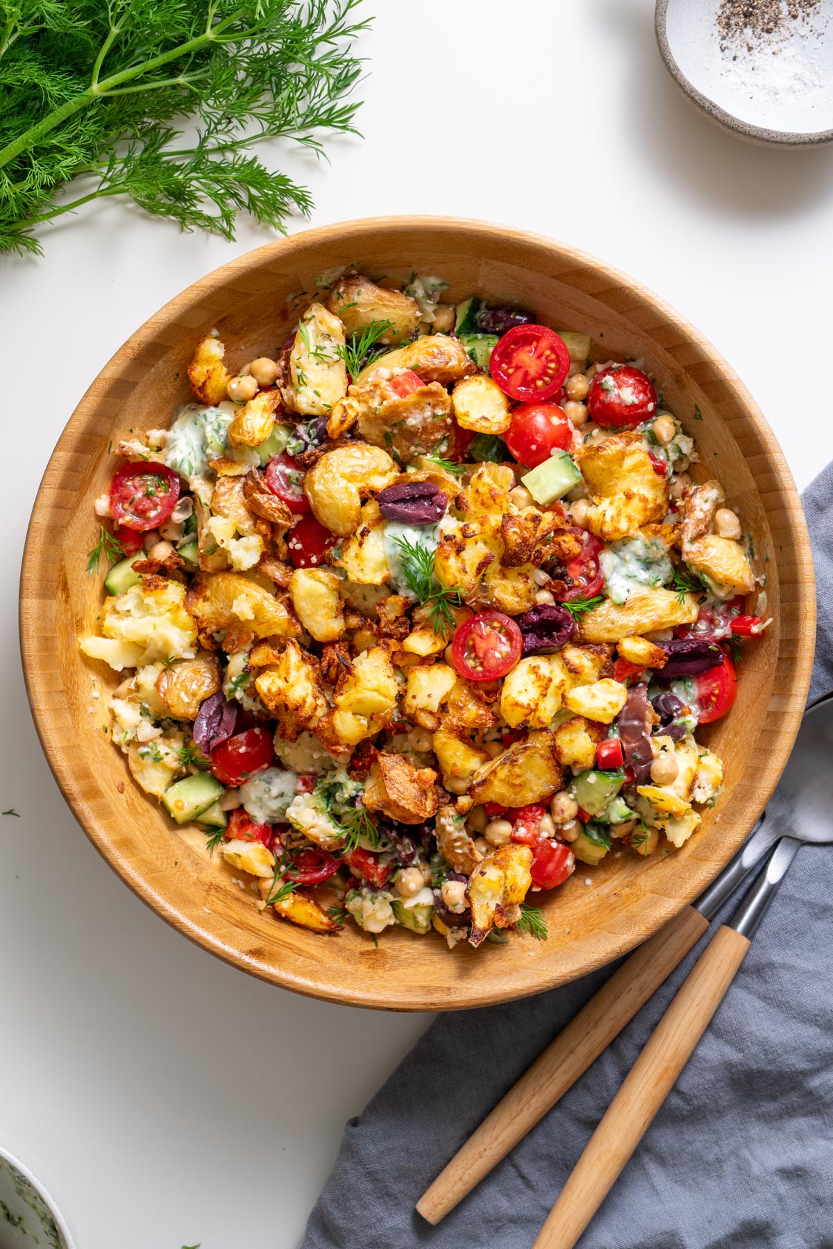 Close-up of Greek-style crispy potato salad showing chickpeas, olives, and tzatziki dressing.