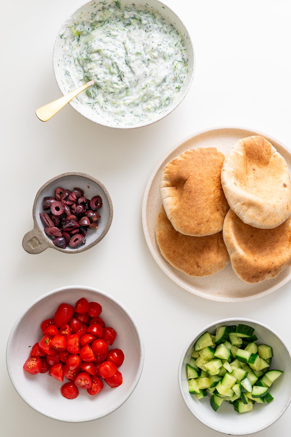 Prepared ingredients including pita bread, chopped cucumbers, tomatoes, olives, and tzatziki for Mediterranean sheet pan pita bowls.