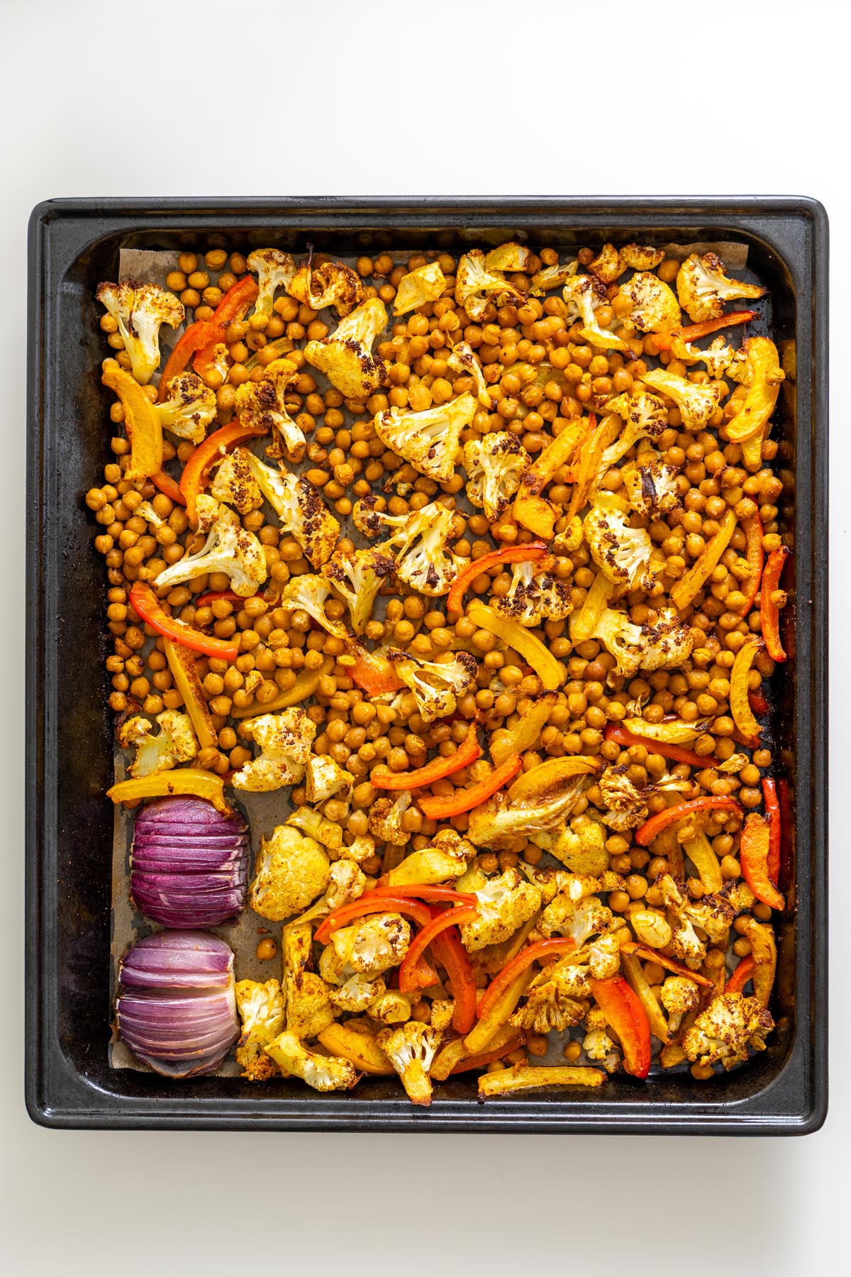 Roasted chickpeas, cauliflower, red onion, and bell peppers on a baking tray for Mediterranean sheet pan pita bowls.