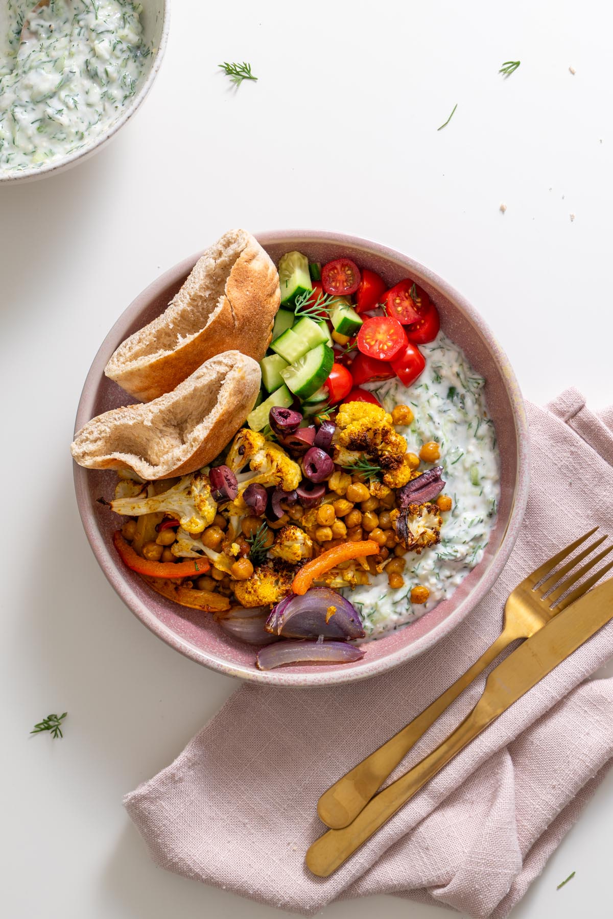 Overhead view of Mediterranean pita bowl with chickpeas, cauliflower, cucumber, tomatoes, olives, and tzatziki.