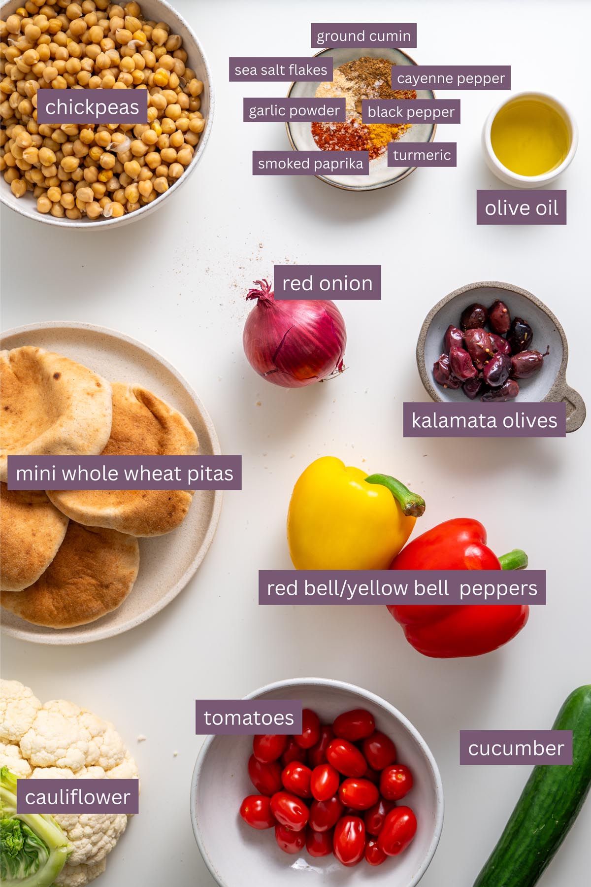 Vibrant ingredients for Mediterranean sheet pan pita bowls with chickpeas, cauliflower, bell peppers, and spices on a white surface.