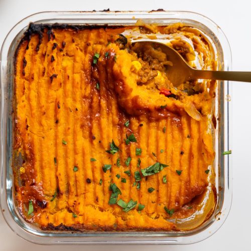 Overhead view of baked Tex Mex Shepherd’s Pie with sweet potato mash topping in a glass dish with spoon