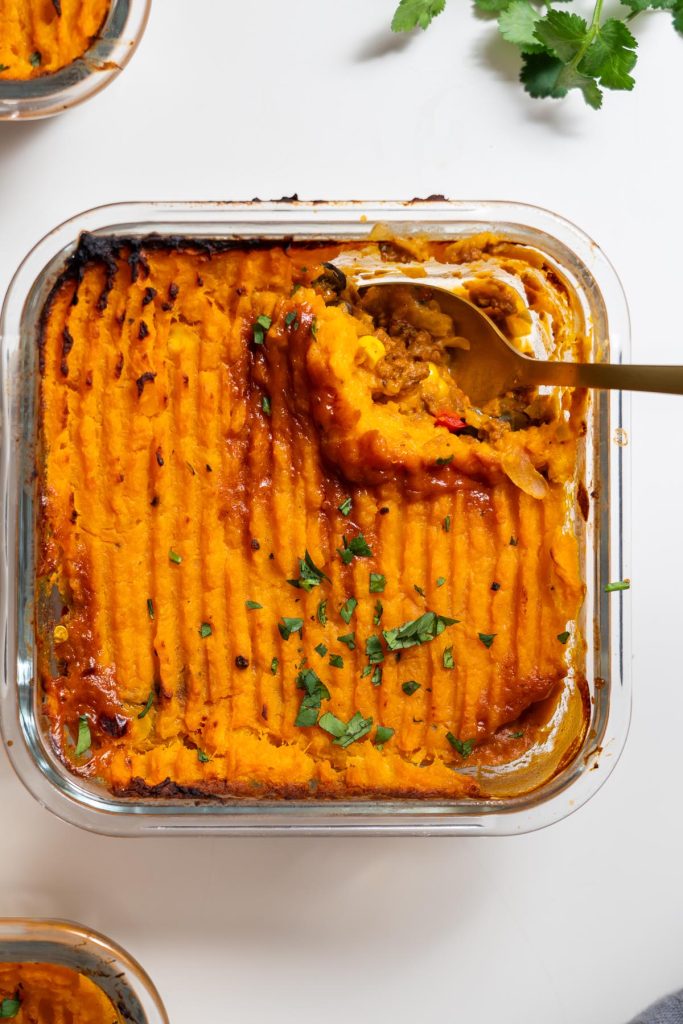 Overhead view of baked Tex Mex Shepherd’s Pie with sweet potato mash topping in a glass dish with spoon