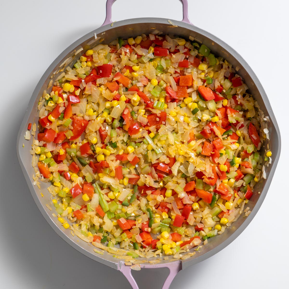 Skillet with diced onions, red bell pepper, celery, and corn sautéing for Tex Mex Shepherd’s Pie on a white surface