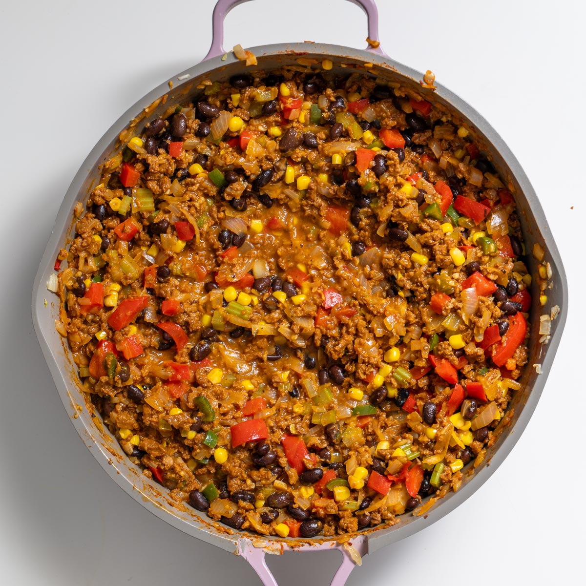 Skillet filled with Tex Mex Shepherd’s Pie filling mixture with corn, black beans, red bell pepper, and vegetables on a white surface