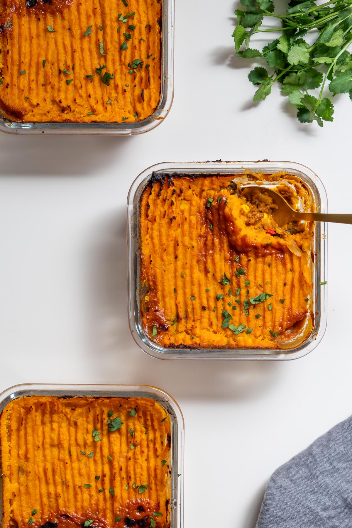Three small glass dishes of baked Tex Mex Shepherd’s Pie with sweet potato mash topping and spoon in center dish