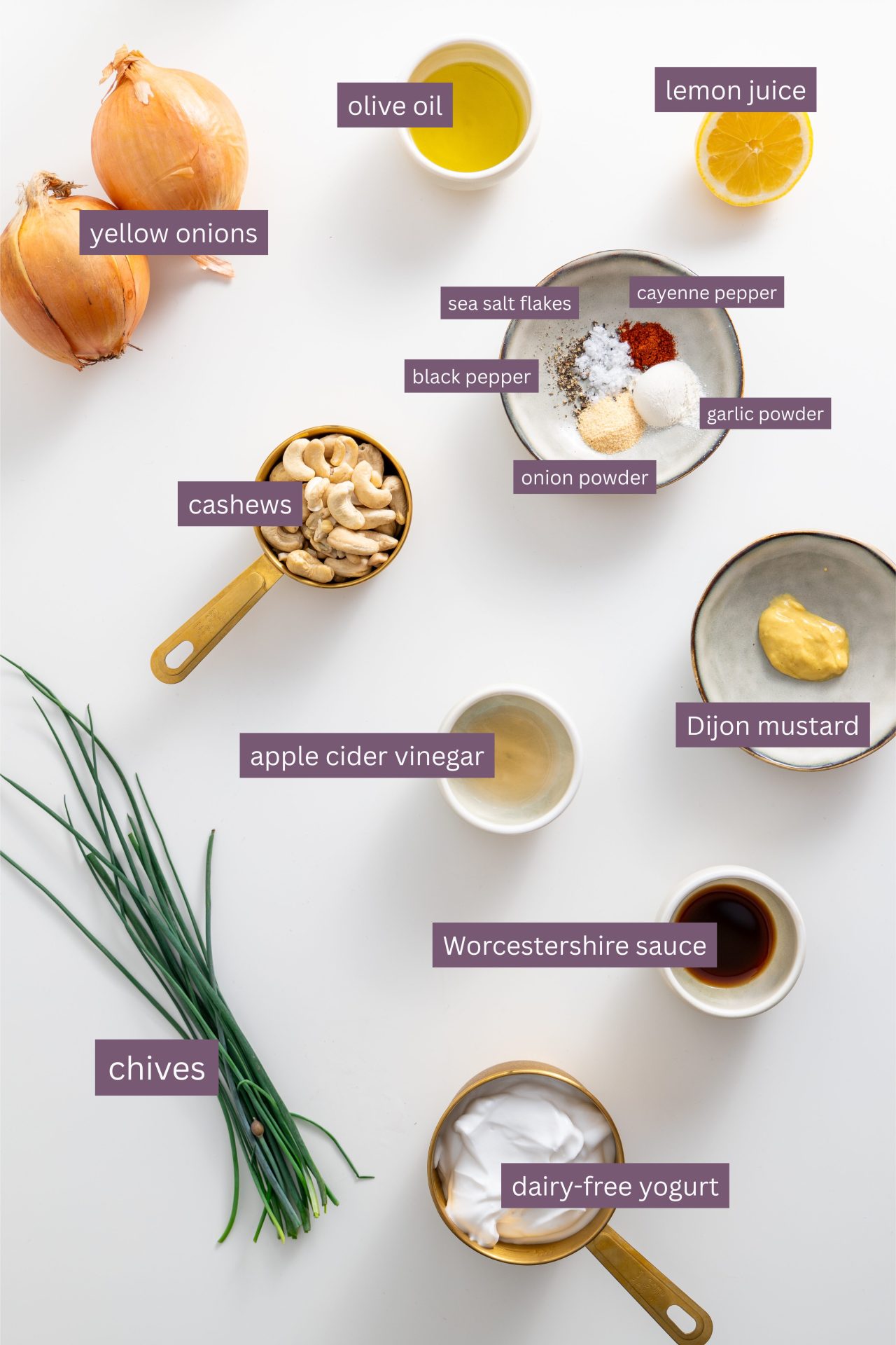 Vibrant ingredients for vegan French onion dip on a white surface, including onions, cashews, yogurt, spices, and herbs