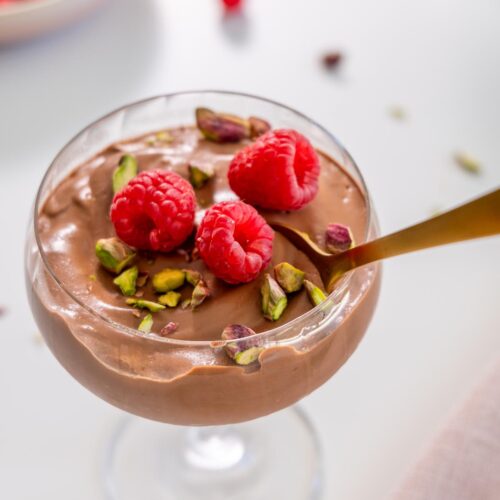 Spoon dipping into chocolate mousse topped with raspberries and pistachios
