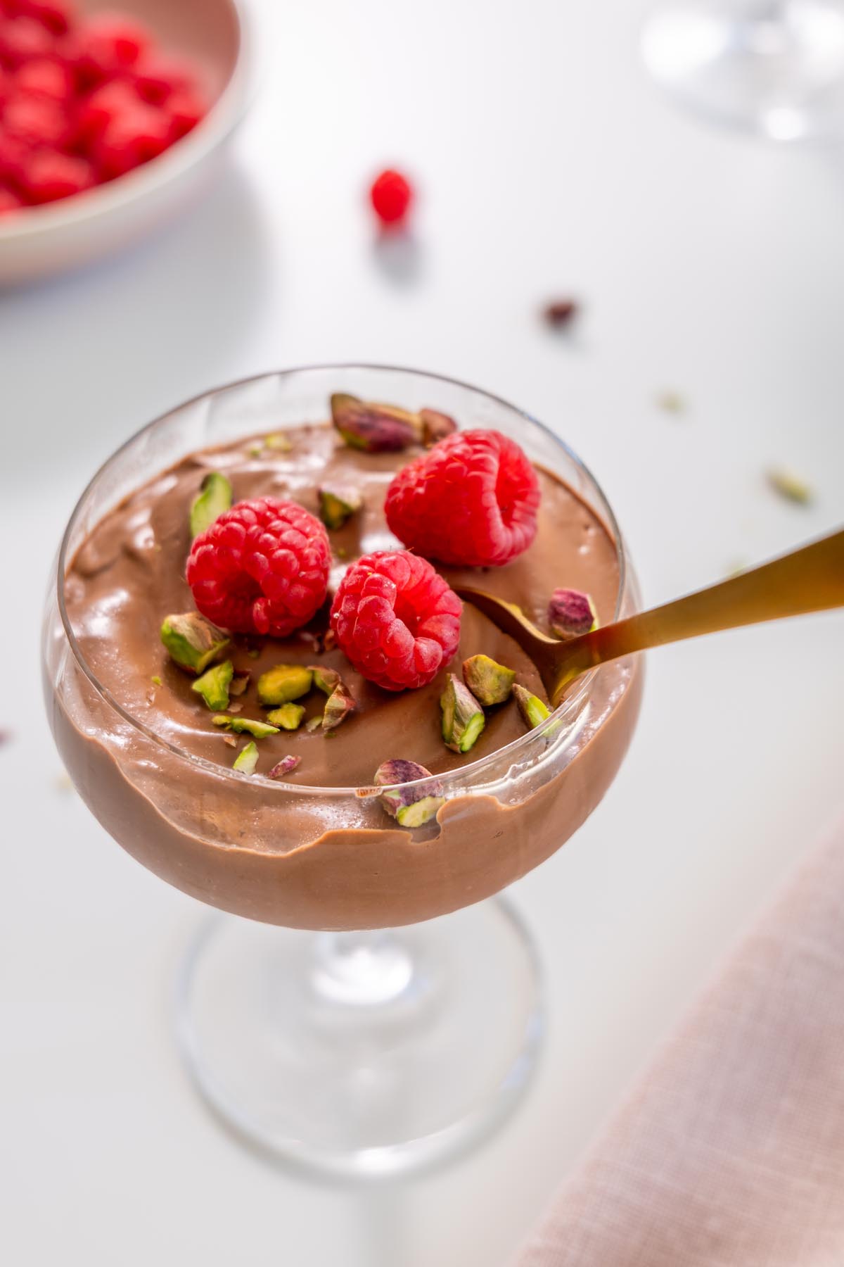 Spoon dipping into chocolate mousse topped with raspberries and pistachios