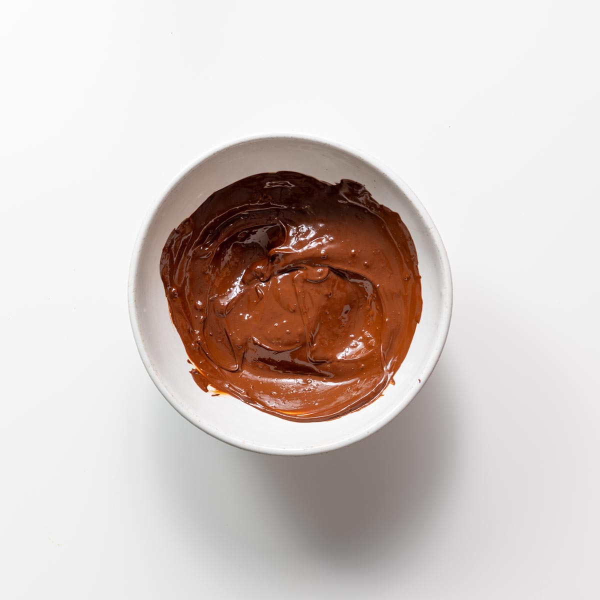 Melted dark chocolate in a white bowl on a white surface