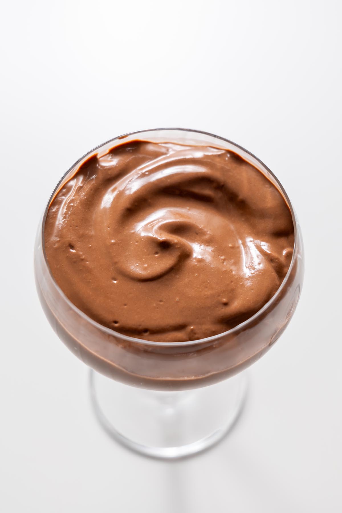 Close up of smooth chocolate mousse in a glass on a white surface