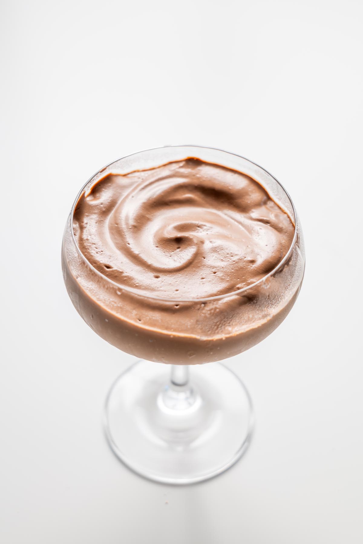Close up of smooth chocolate mousse in a glass on a white surface
