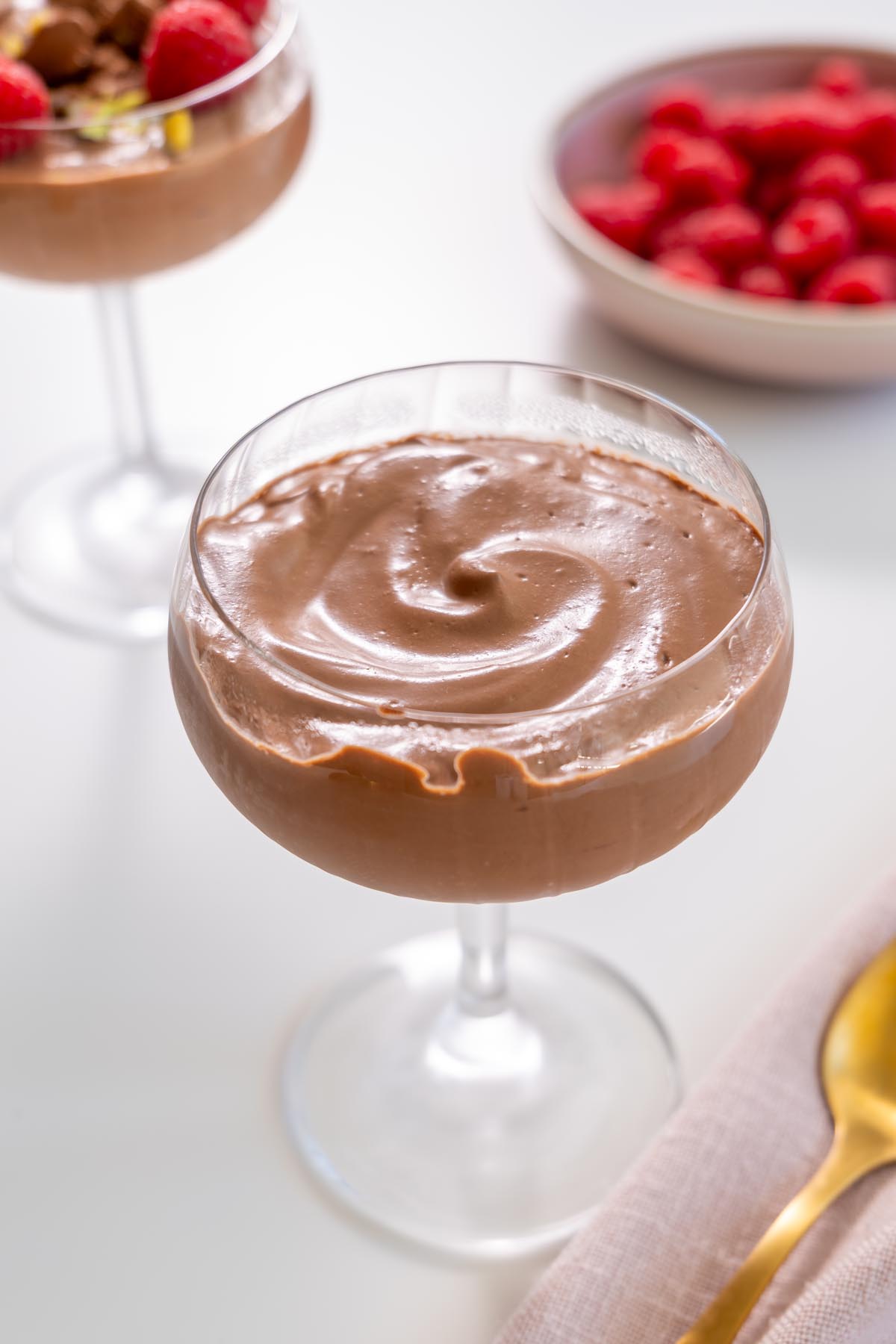Chocolate mousse in a glass with raspberries in the background on a bright surface