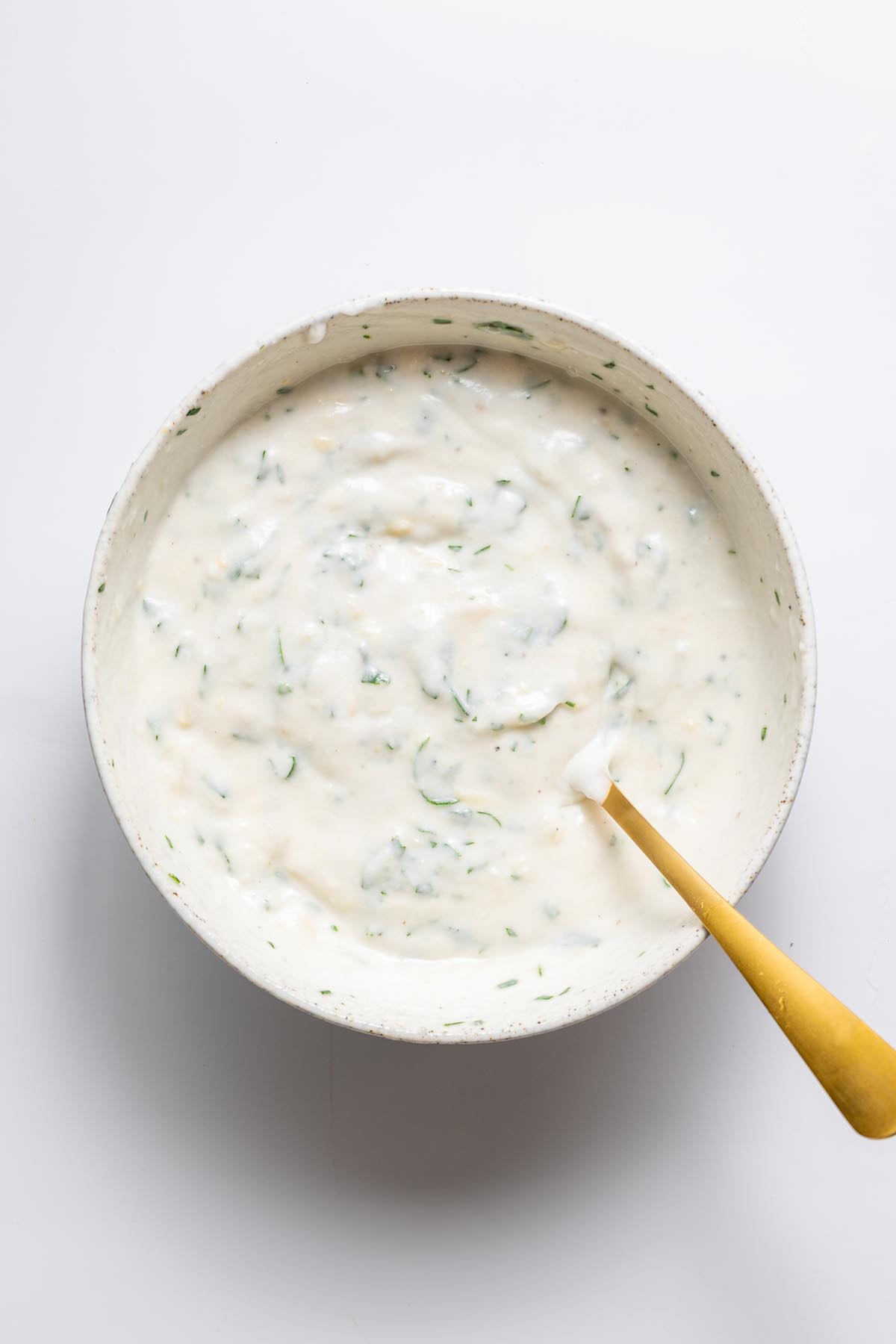 Creamy garlic yogurt sauce mixed with parsley in a white bowl with a gold spoon.