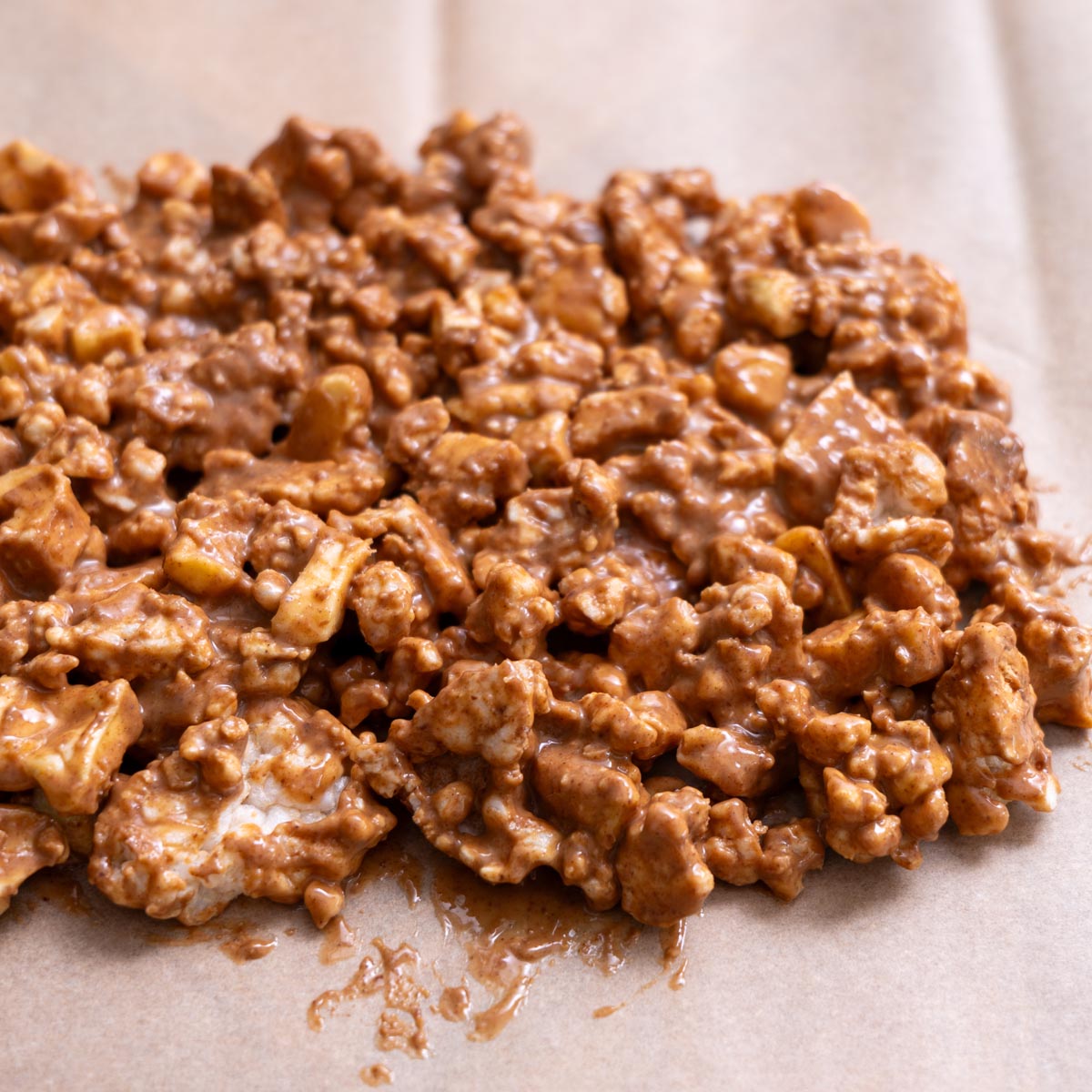 Close-up of mixture for crispy apple chocolate bark made of crumbled rice cakes, dried apple slices and almond butter on parchment paper