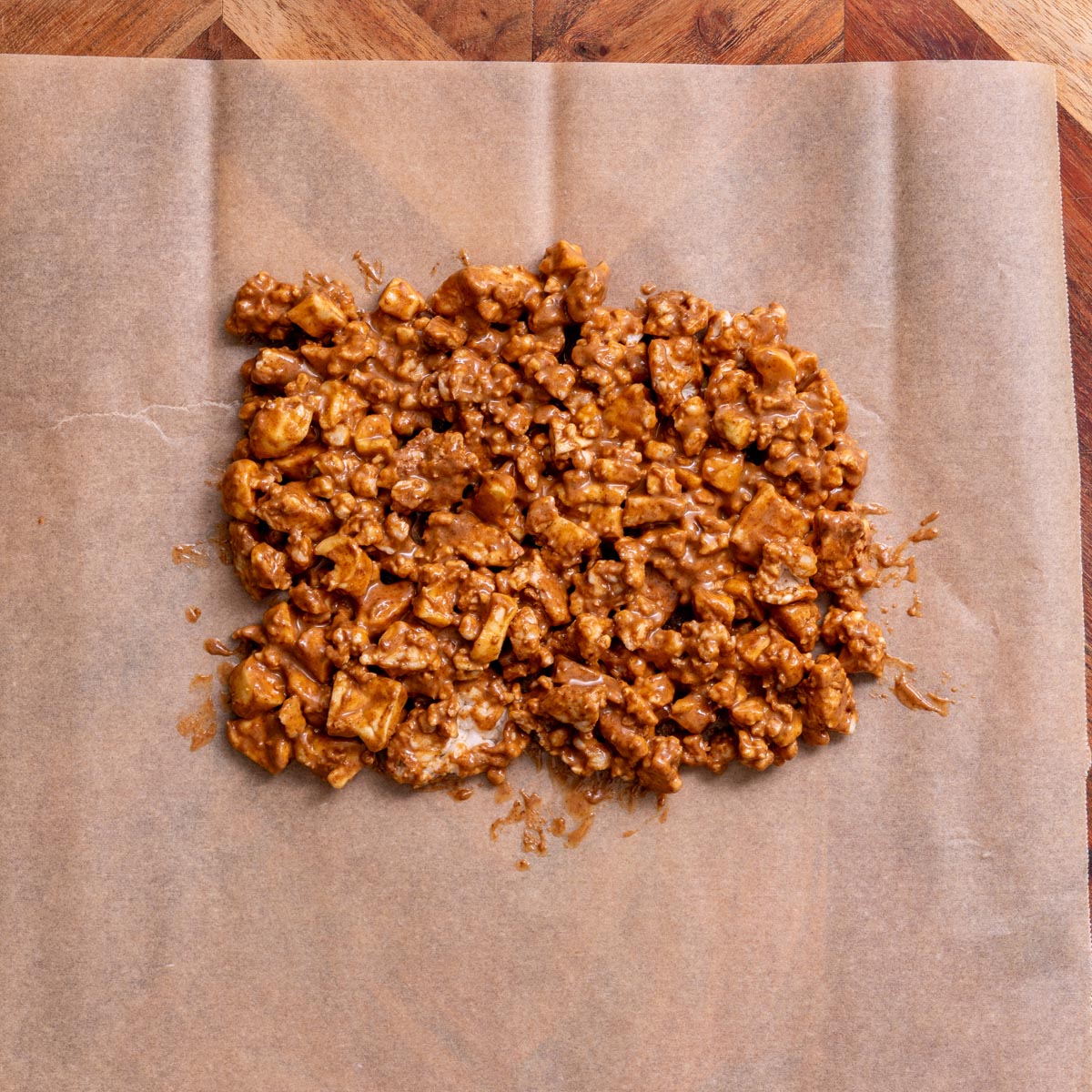 Mixture of crumbled rice cakes, dried apple slices, almond butter and cinnamon on parchment paper for crispy apple chocolate bark