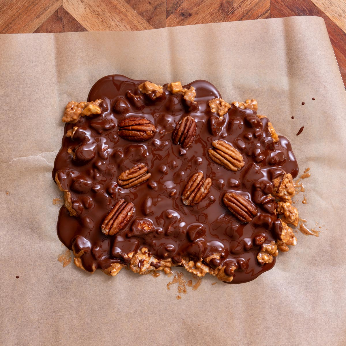 Whole slab of crispy apple chocolate bark with melted chocolate and pecans on parchment paper on wooden board